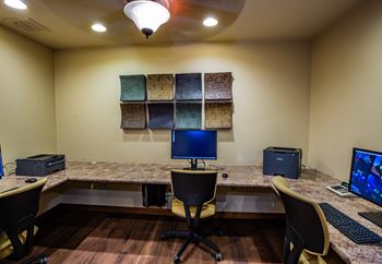 A room with a desk, chairs, and two monitors.